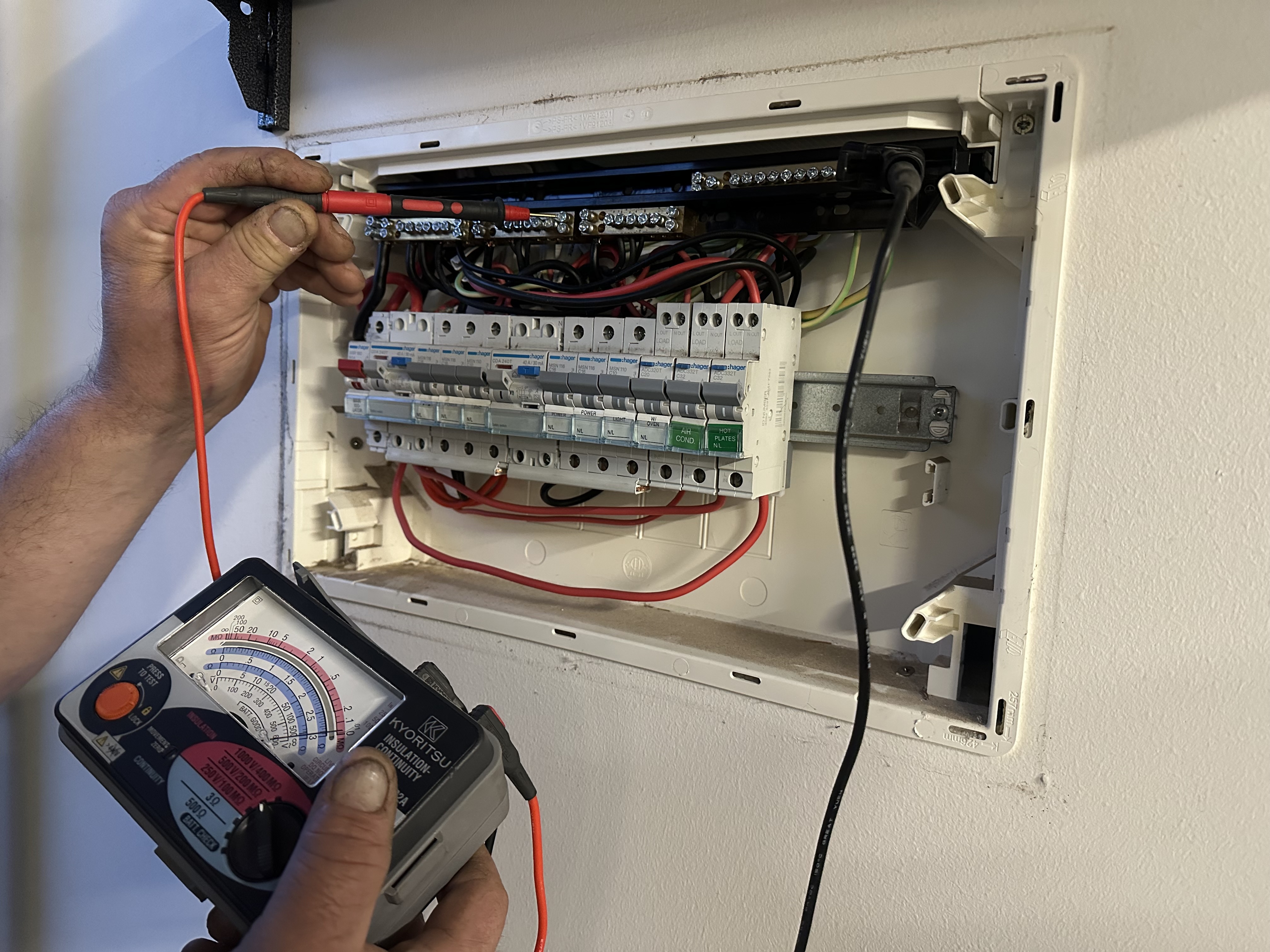 Electrician using a multimeter to test a switchboard for faults